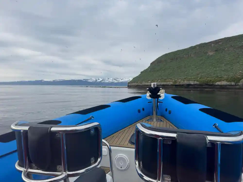Blue boat bow in foreground facing green cliffs and mountains