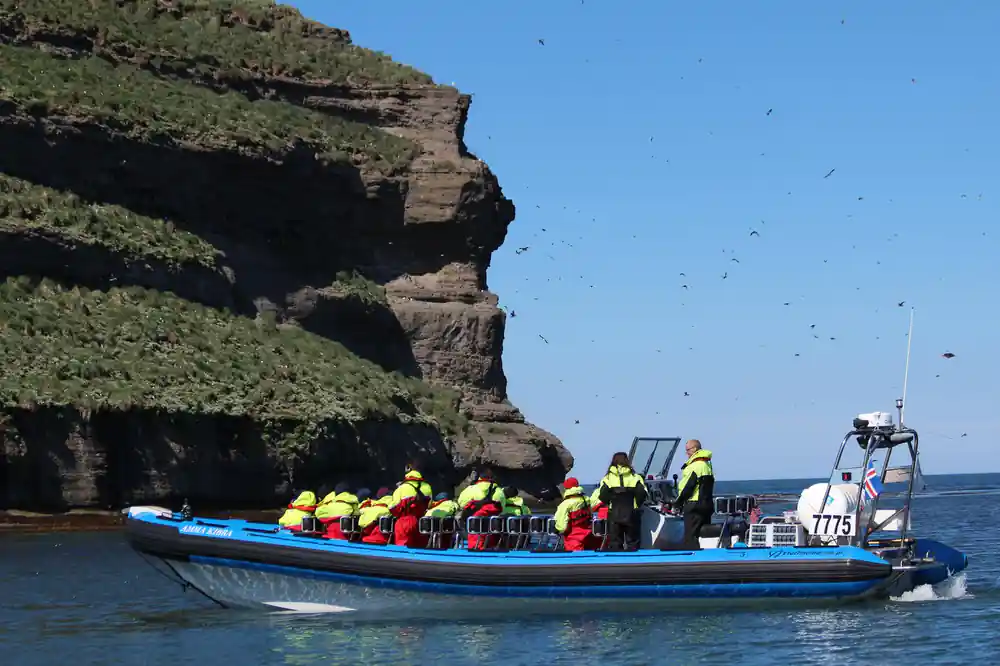Boat at cliff base with tourists in yellow jackets