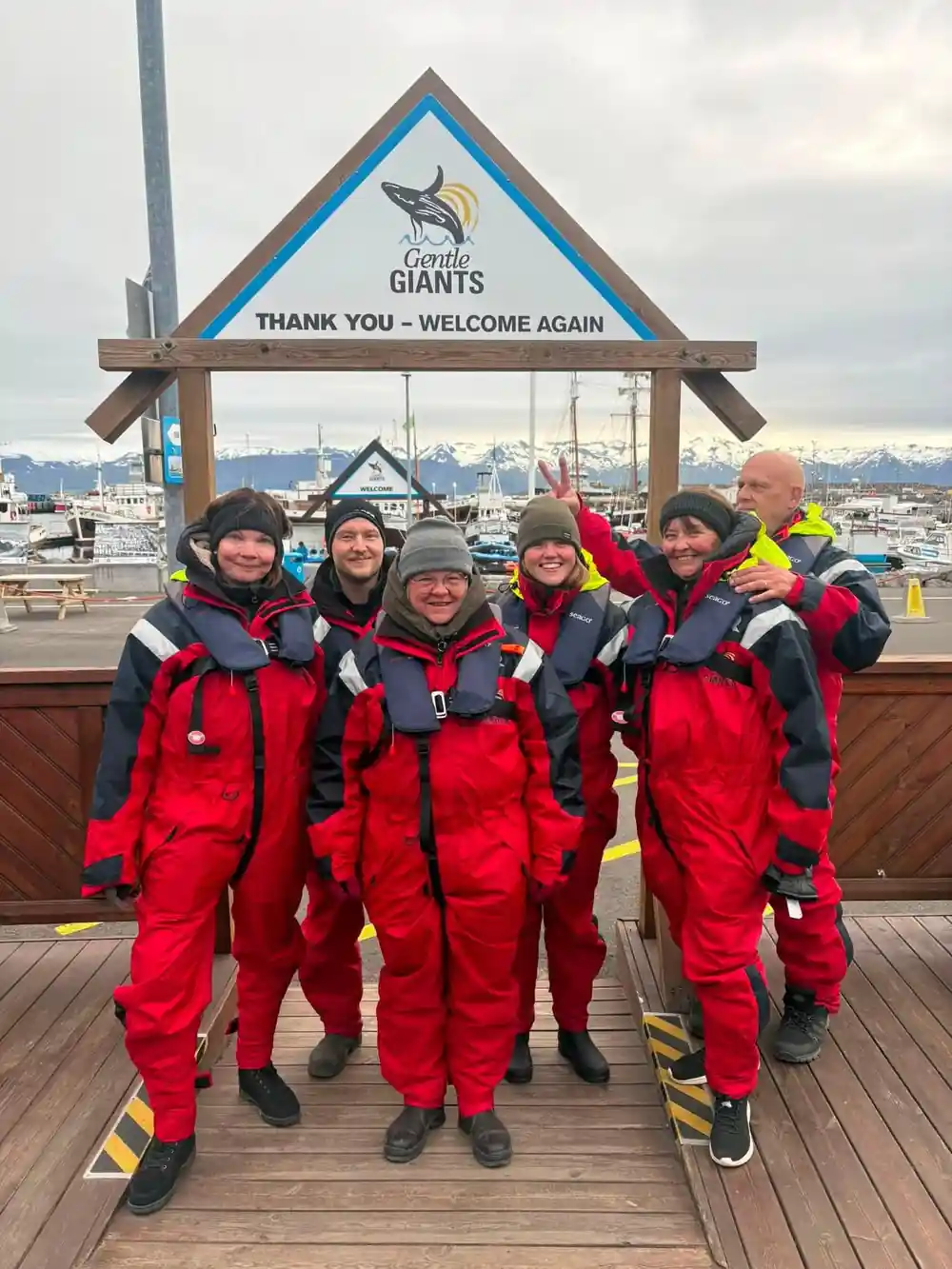 Group of people in red wetsuits at whale watching sign