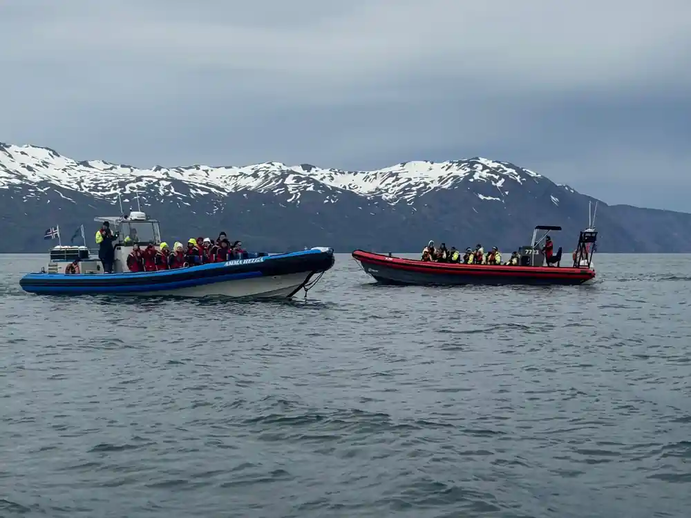 Two boats full of people with snow-capped mountains behind